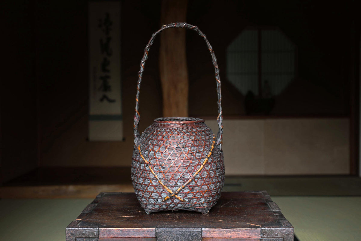 A traditional Japanese woven basket with a handle, placed on a wooden surface against a dark background.