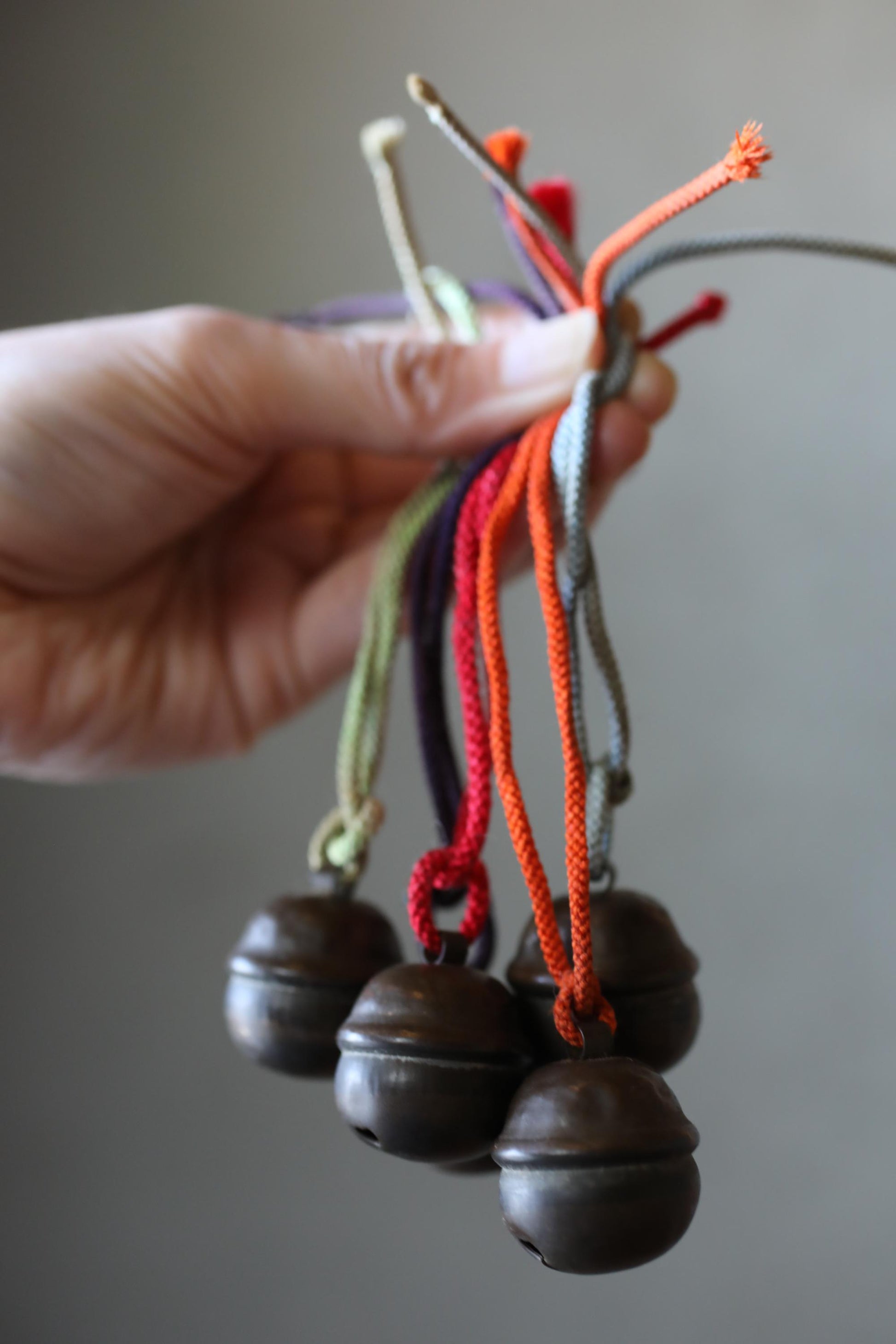 A hand is holding a bunch of colorful bells, including black, red, and orange ones, against a gray background.