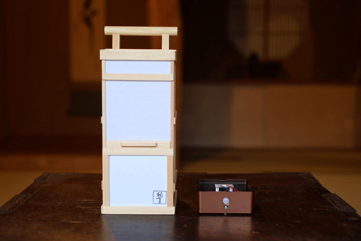 A wooden lantern with a white paper attached to it, placed next to a small brown box on a wooden surface.