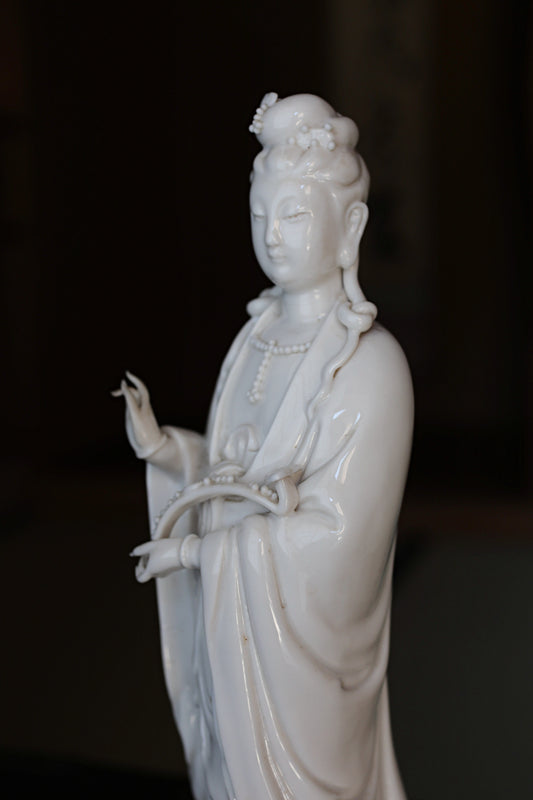 A white porcelain figurine of a female deity, possibly a goddess or deity, with an ornate headdress and holding a musical instrument.