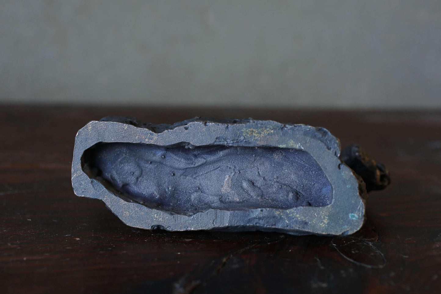 A dark, metallic object resembling a piece of metal or a sculpture is shown on a dark wooden surface.