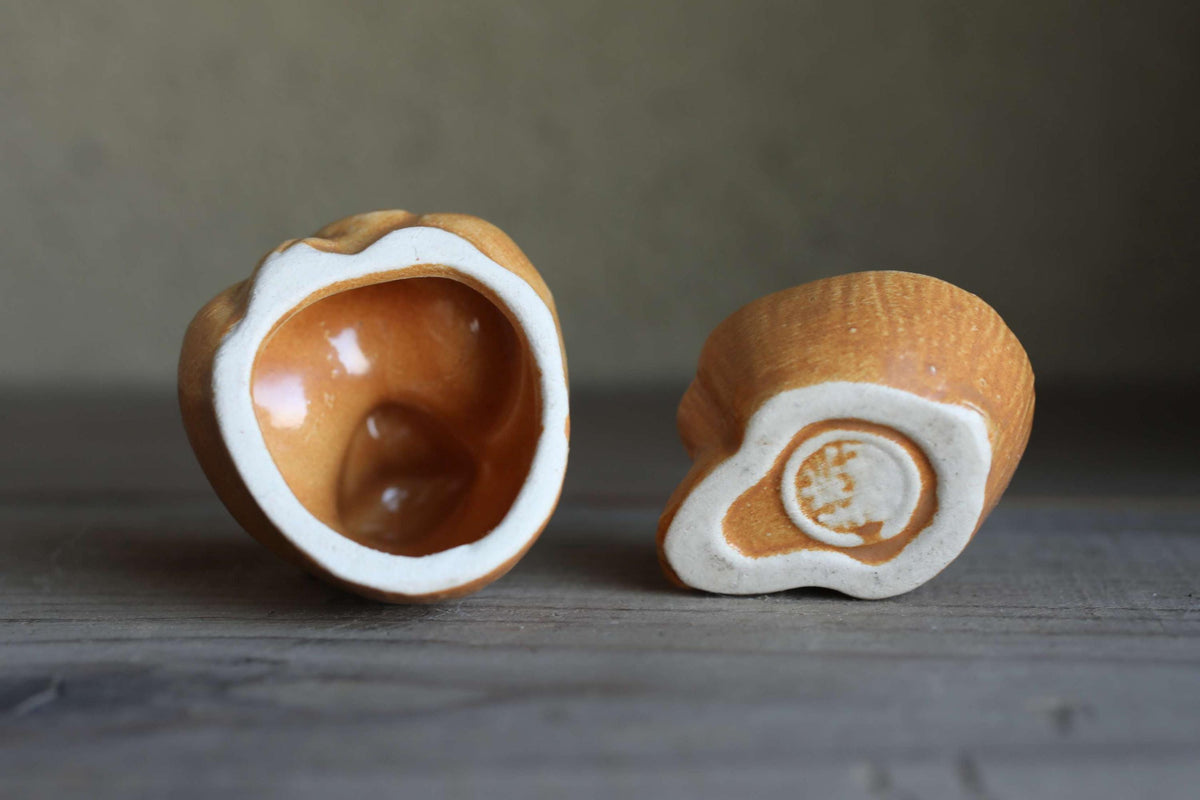 Two ceramic objects, one with a white interior and the other with a white exterior, are placed on a wooden surface.