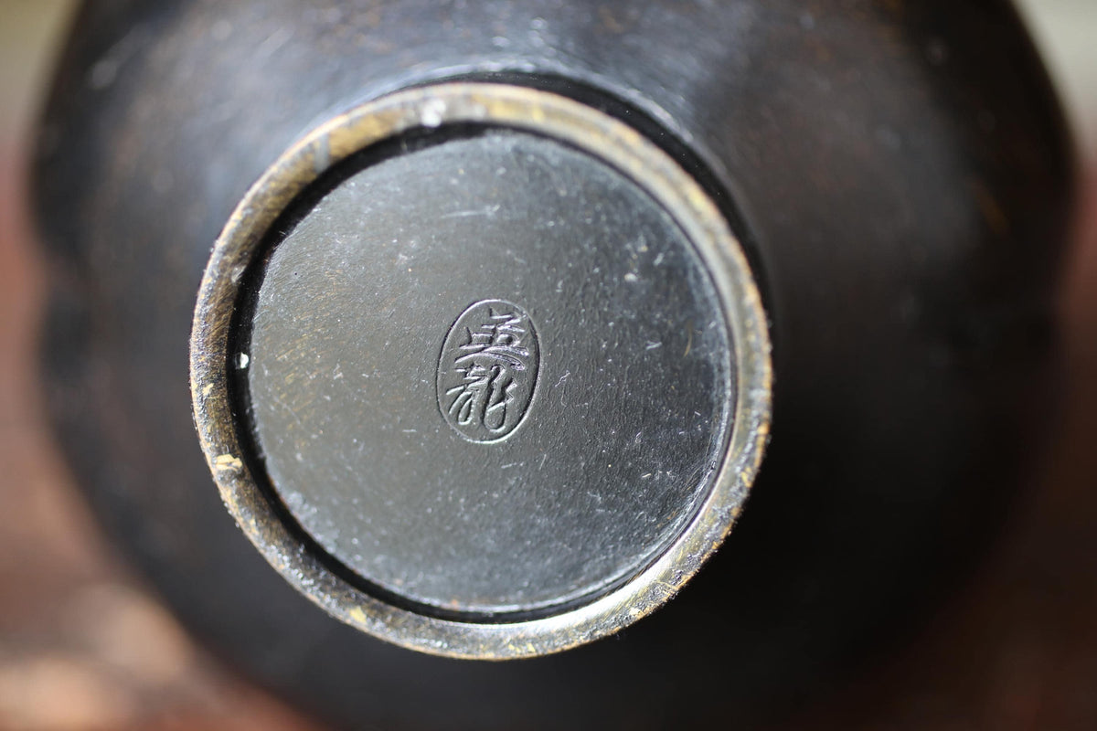 A close-up image of the bottom part of a black ceramic object, possibly a bowl or vase, with a distinctive logo or emblem on it.