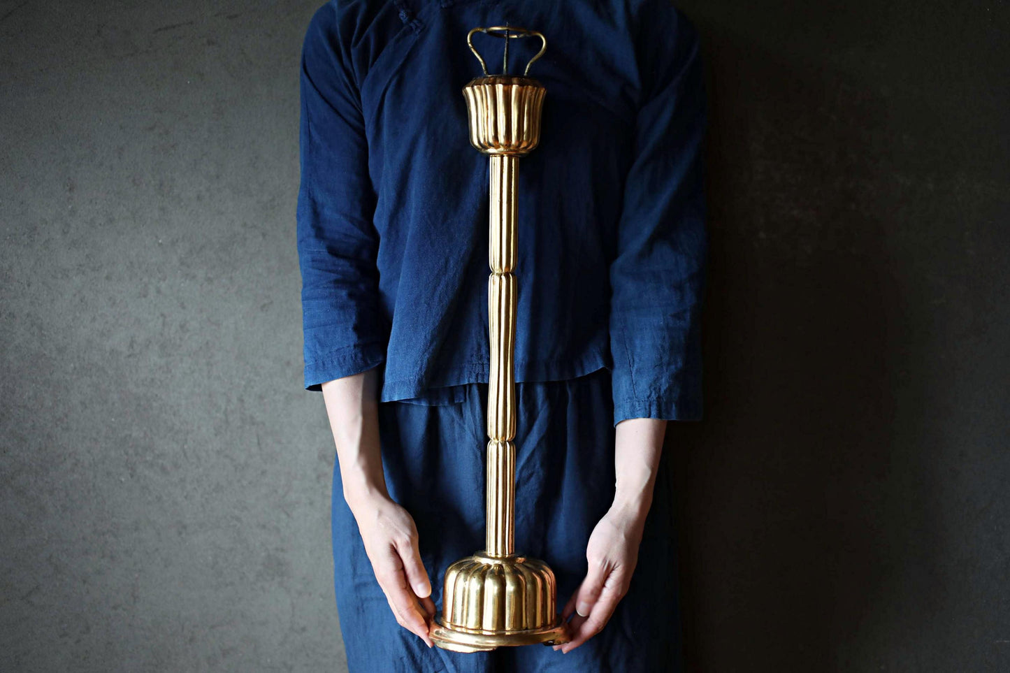 A person wearing a blue shirt is holding a tall, ornate golden object, which appears to be a decorative piece or a trophy.