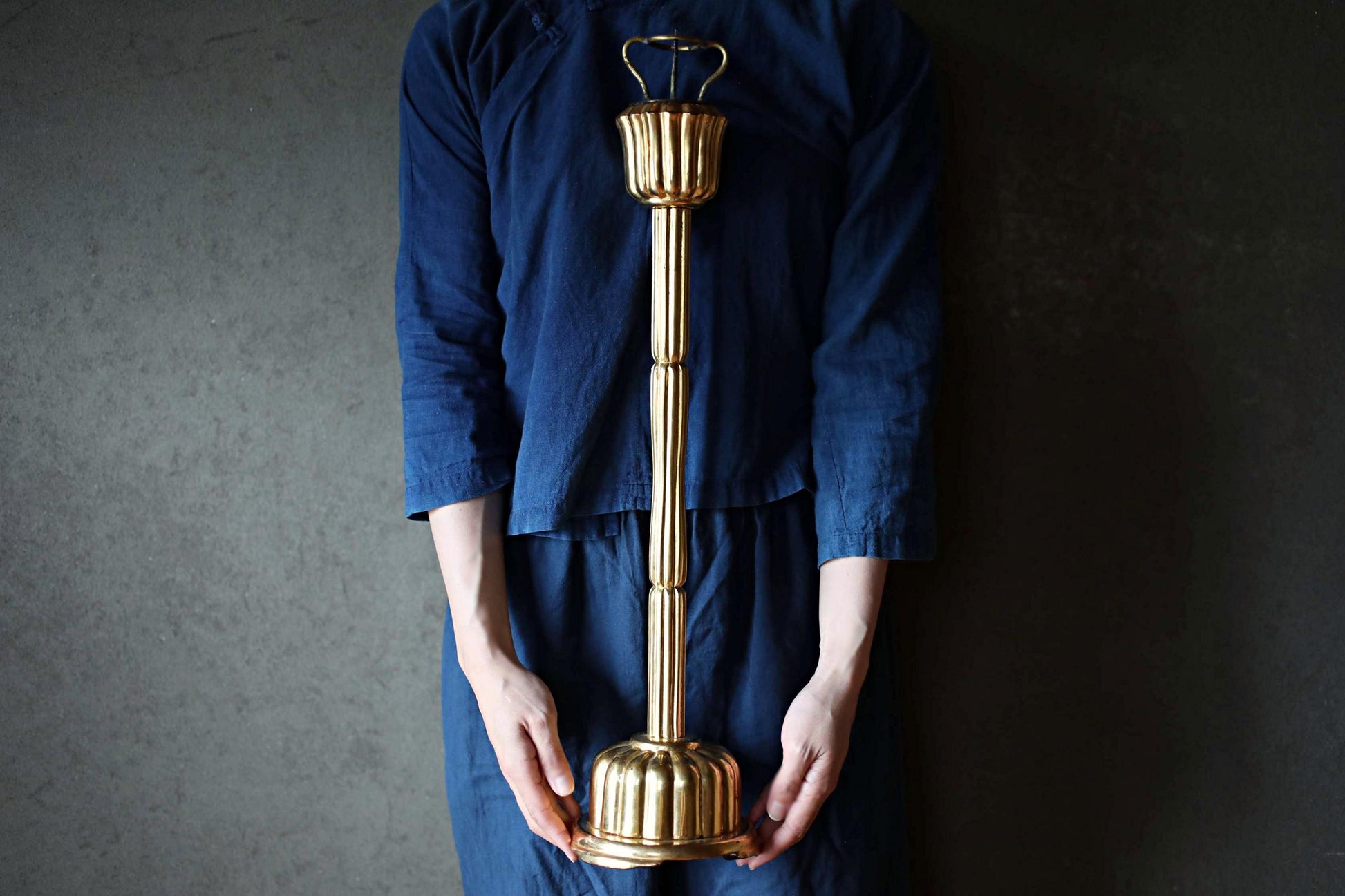 A person wearing a blue shirt is holding a tall, ornate golden object, which appears to be a decorative piece or a trophy.