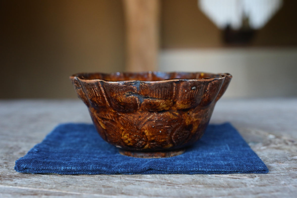 A brown ceramic bowl with a scalloped edge sits on a blue cloth on a wooden surface.