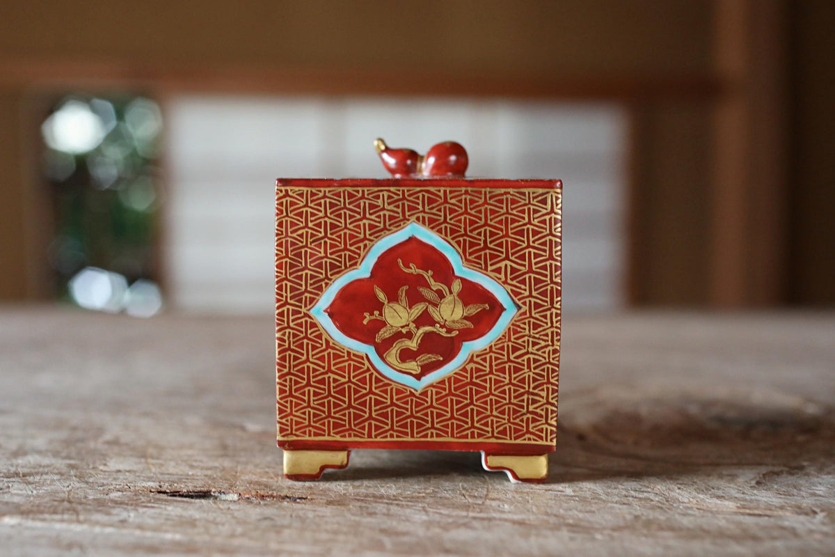 A red and gold decorative box with a bird motif on the front, placed on a wooden surface.