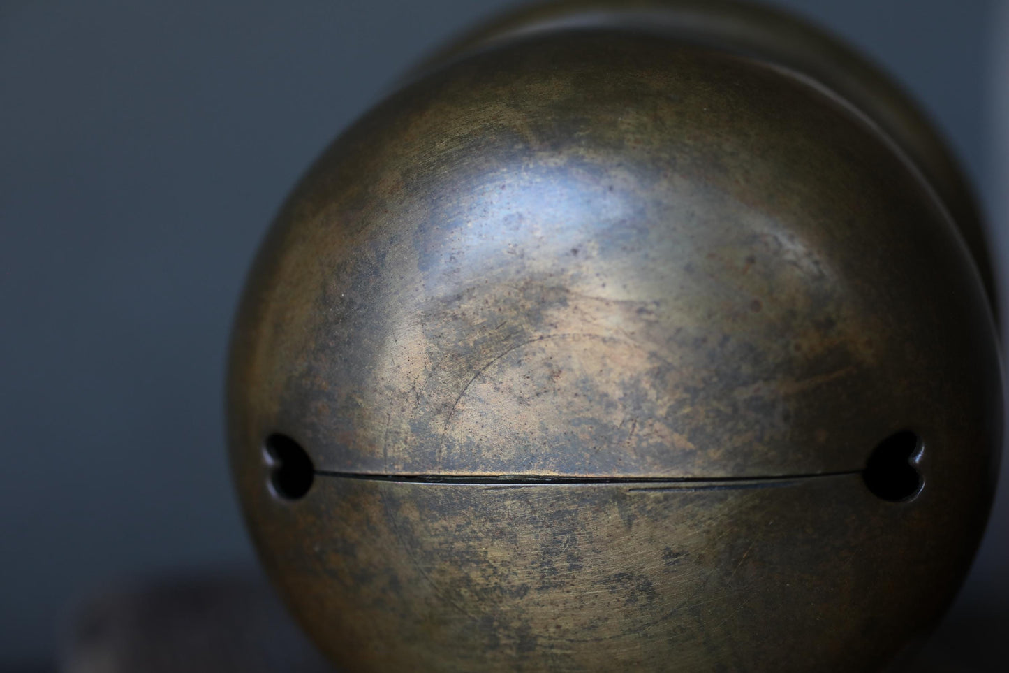 A close-up view of a metal bell or ornament with a textured surface and a hole in the center.