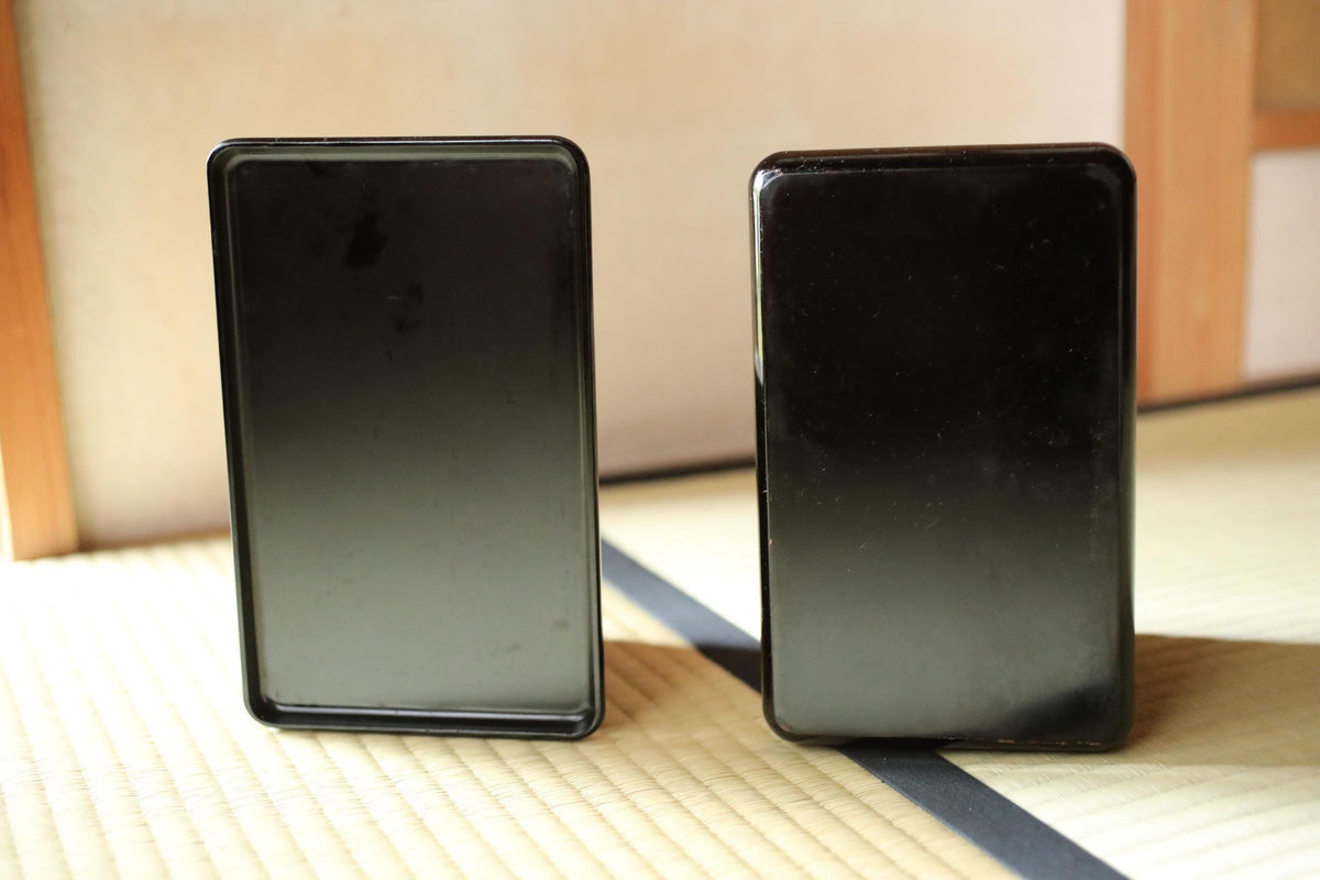 Two black rectangular objects are placed side by side on a wooden surface.