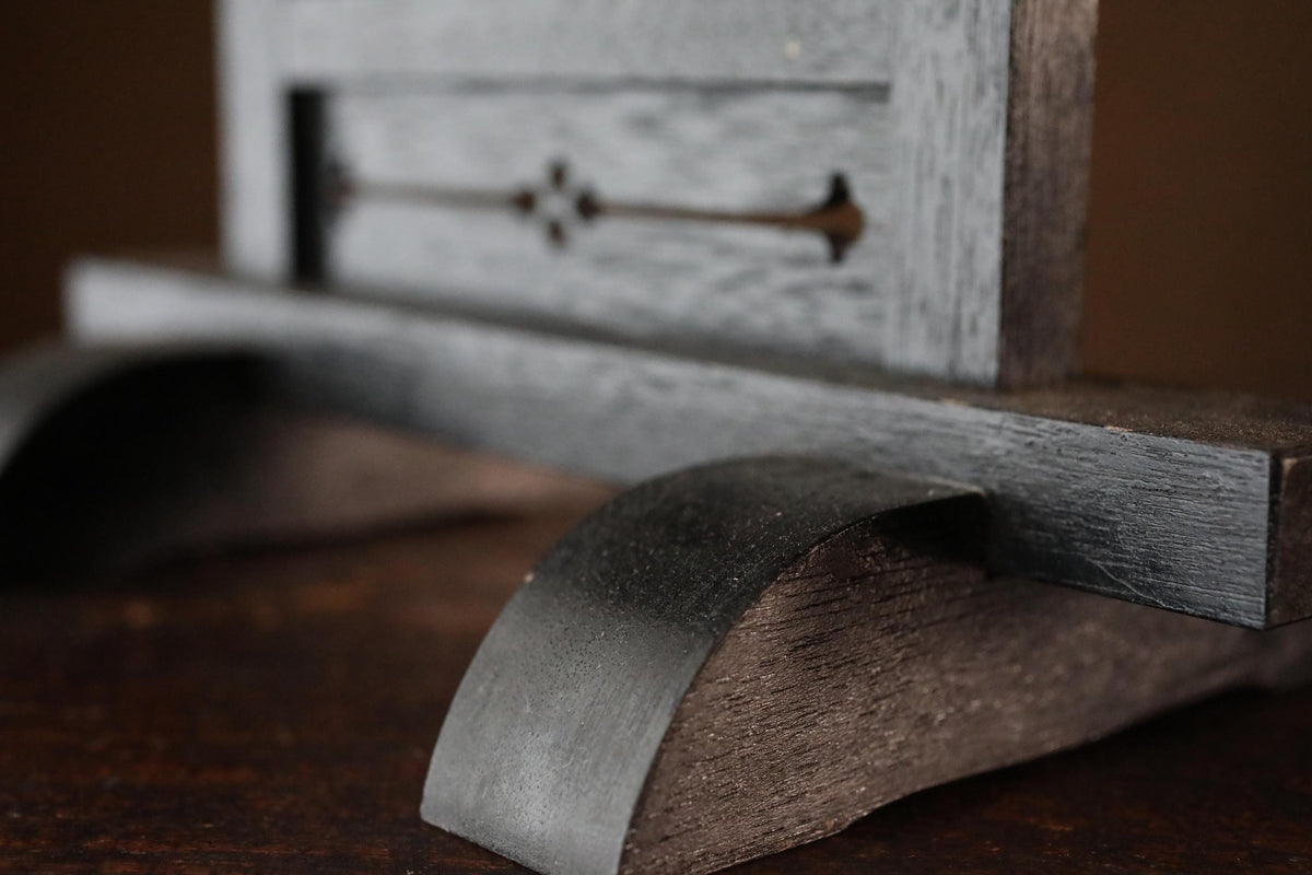 a close-up view of a wooden object, possibly a piece of furniture or a decorative item, with a dark, textured surface.