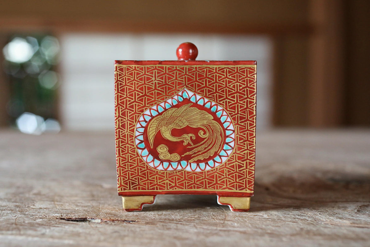 A red and gold decorative box with a gold bird design on the front, placed on a wooden surface.