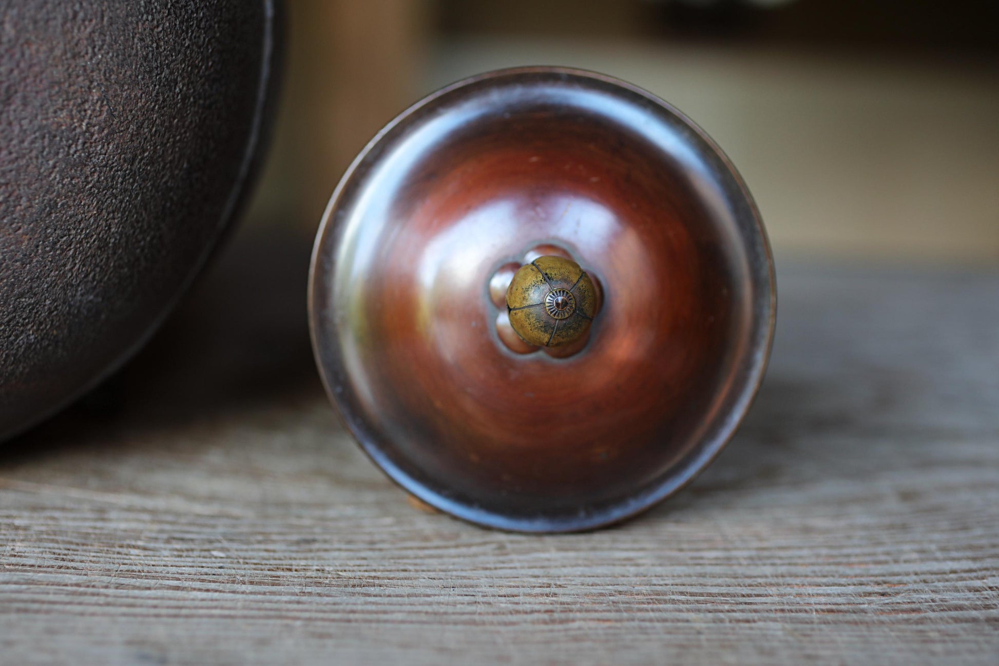 A close-up image of a round, metallic object with a flower-like design on its surface, resting on a wooden surface.