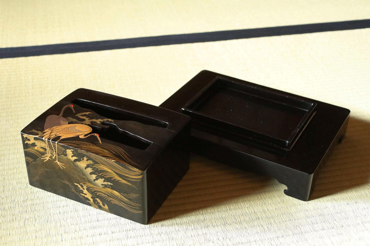 a black box with a gold design depicting a crane on a wave, placed on a white surface.