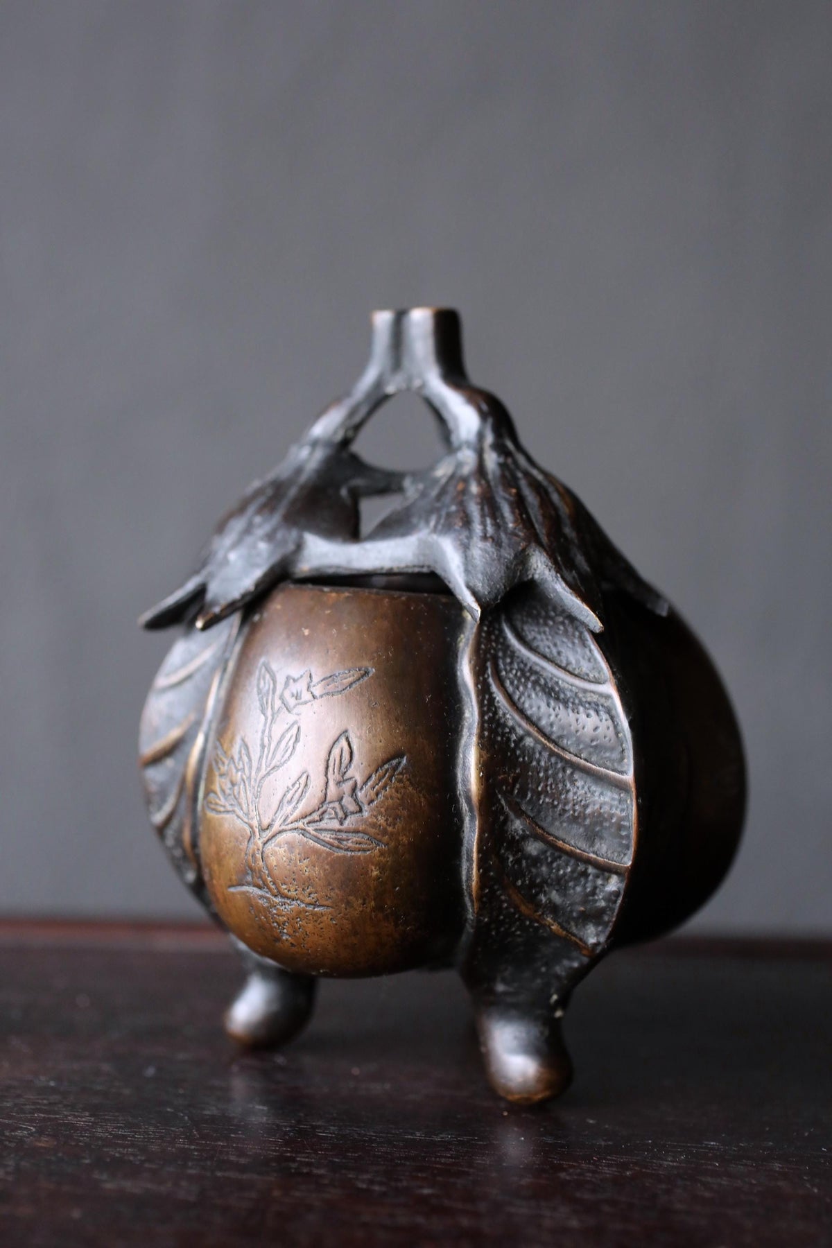 A bronze incense burner with a leaf design on the front sits on a dark surface.