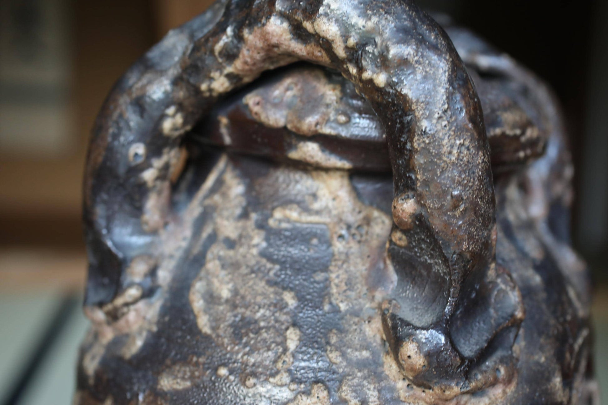 A close-up view of a dark, textured ceramic object with a curved handle, possibly a vase or container.