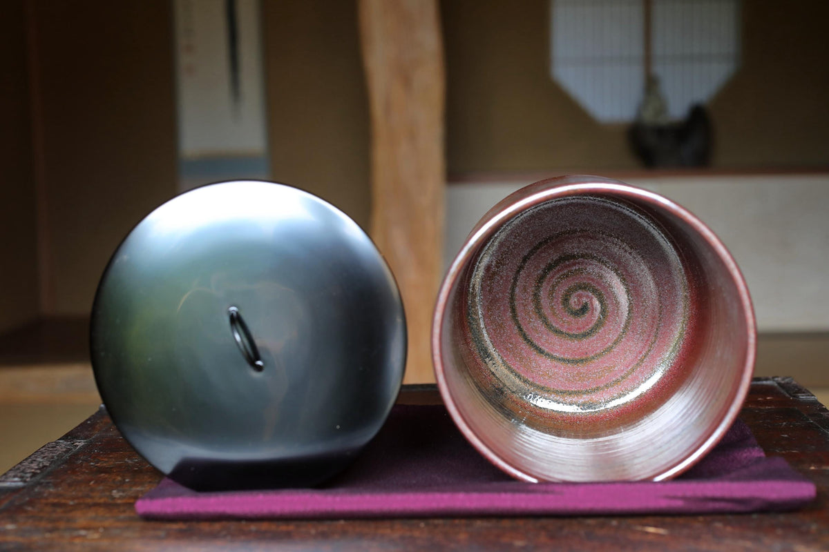 two ceramic cups, one with a spiral pattern and the other with a plain design, placed on a purple cloth on a wooden surface.