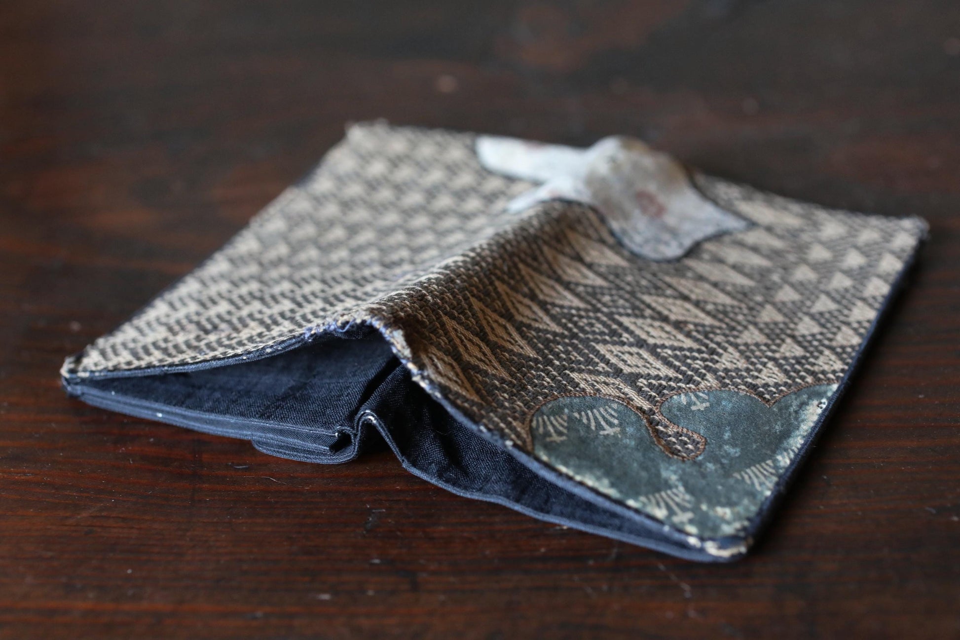 A folded wallet with a patterned design sits on a wooden surface.