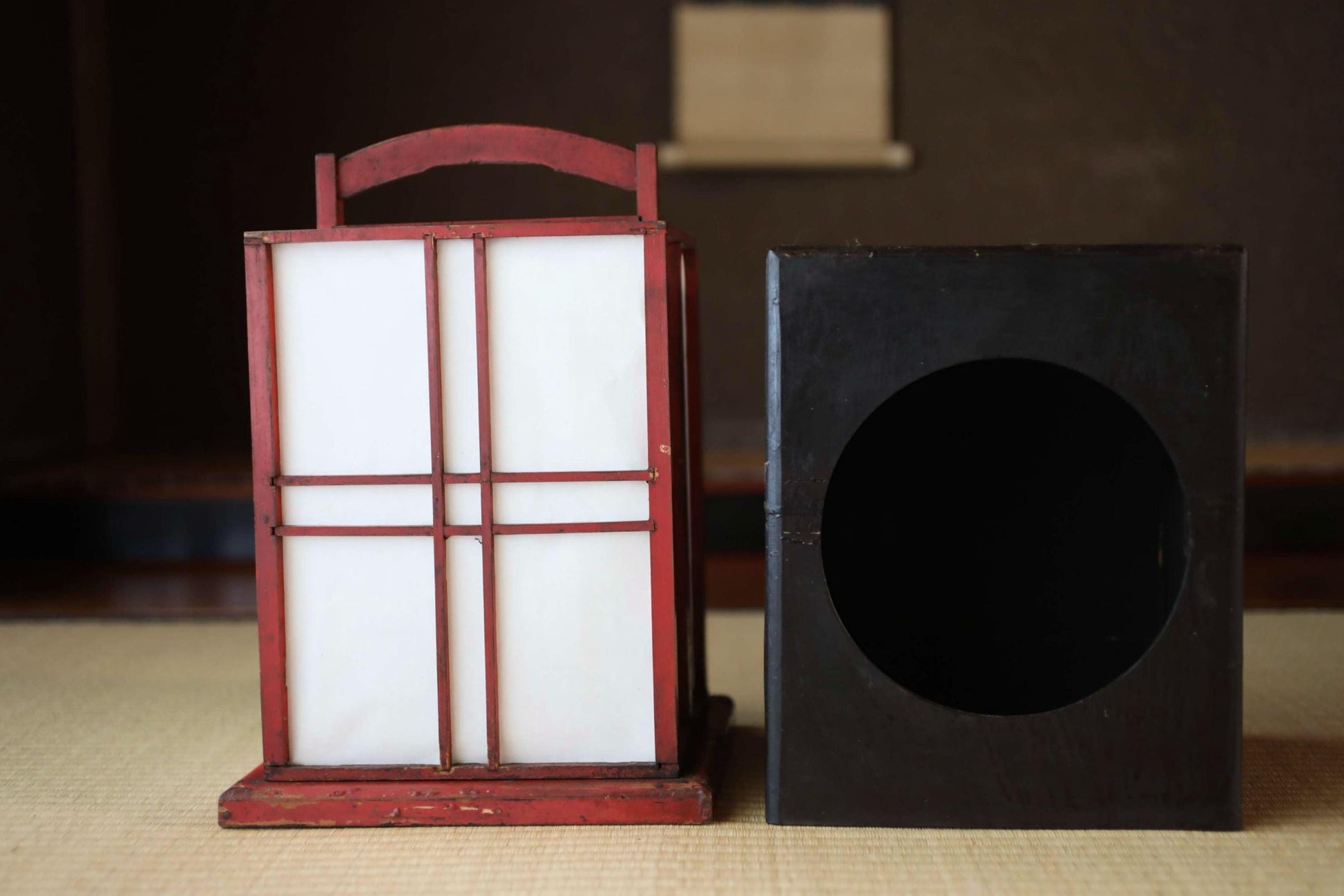 a red lantern with a white interior and a black lantern with a circular opening, both sitting on a wooden surface.
