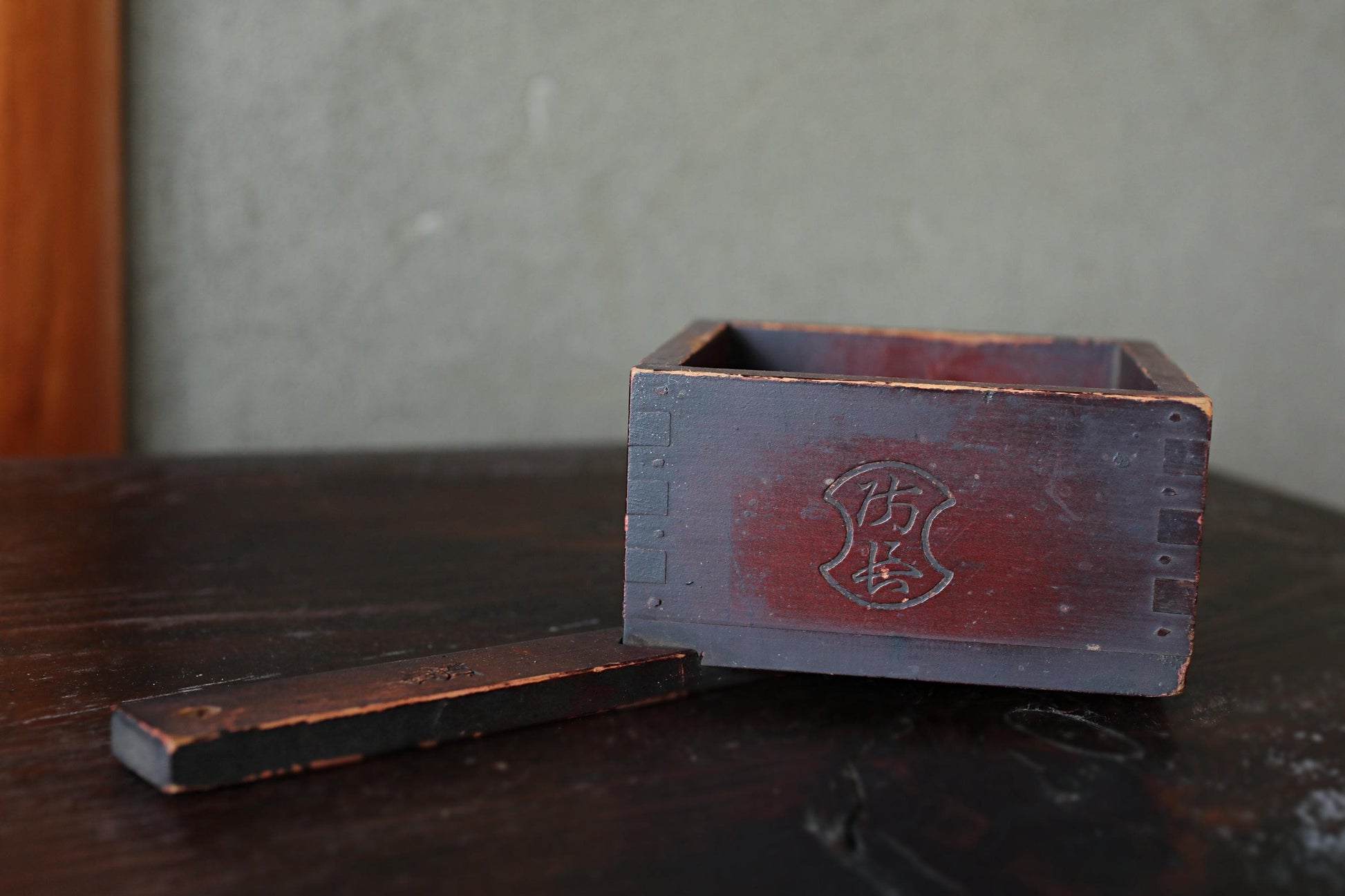 An old, weathered wooden box with a carved design on its side, sitting on a dark wooden surface.