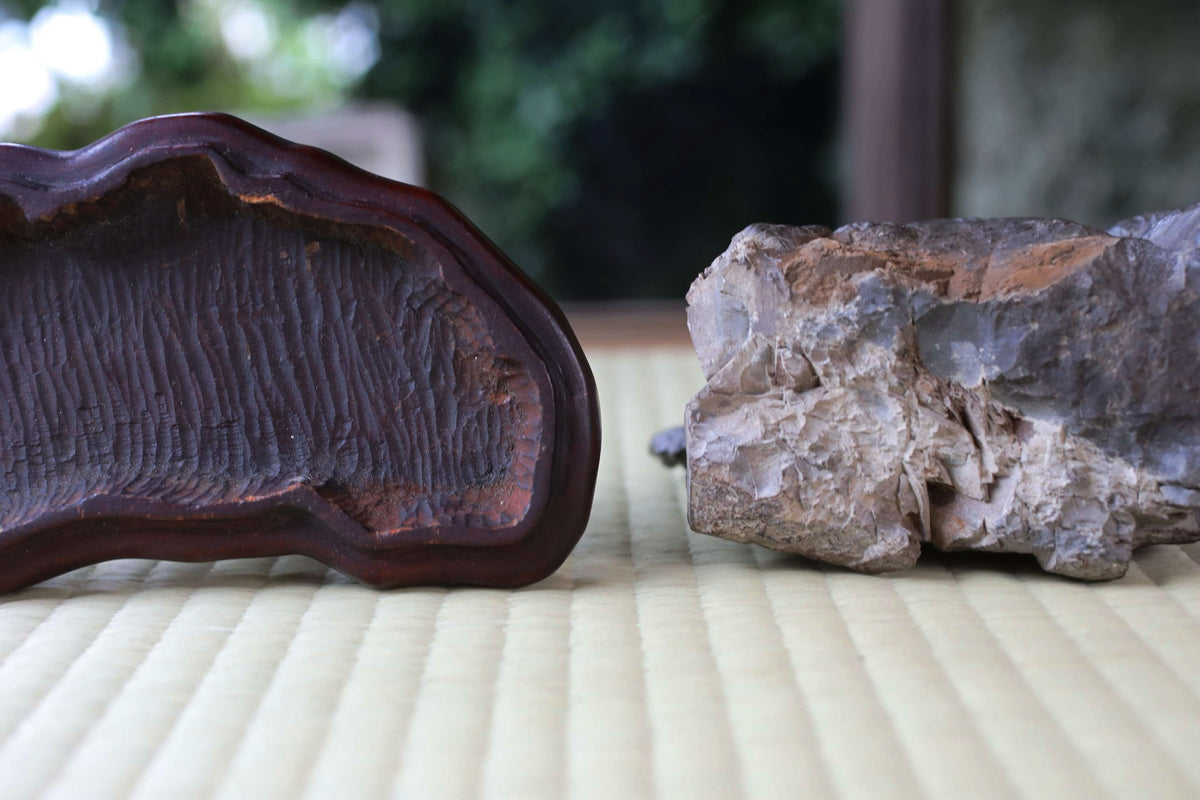 two distinct objects placed on a textured surface, one being a dark-colored wooden object and the other a large, irregularly shaped rock.