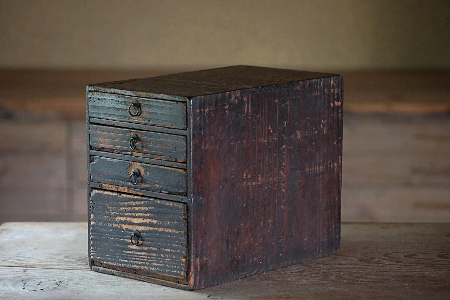 An old, weathered wooden drawer with four smaller drawers, sitting on a wooden surface.