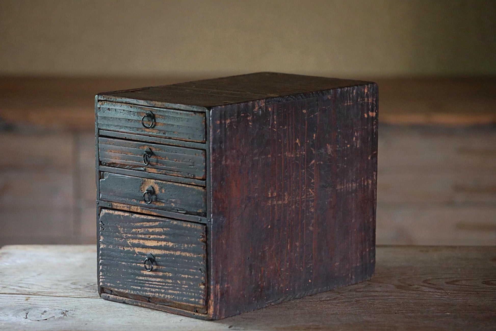 An old, weathered wooden drawer with four smaller drawers, sitting on a wooden surface.