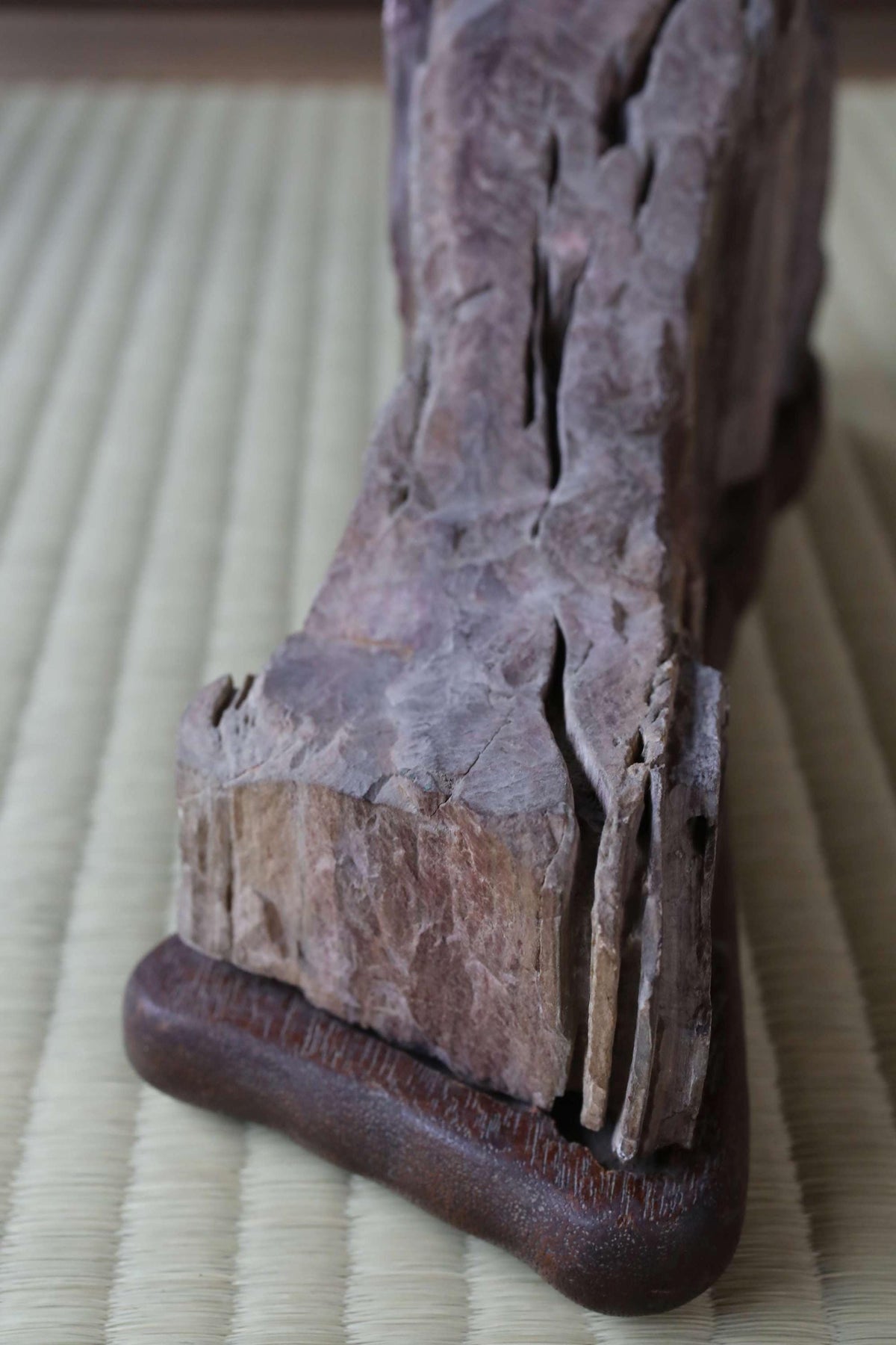 a close-up view of a piece of wood with a rough, textured surface, resting on a woven mat or mat-like material.
