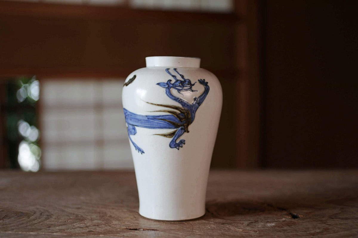 A white ceramic vase with a blue dragon design on it, sitting on a wooden surface.