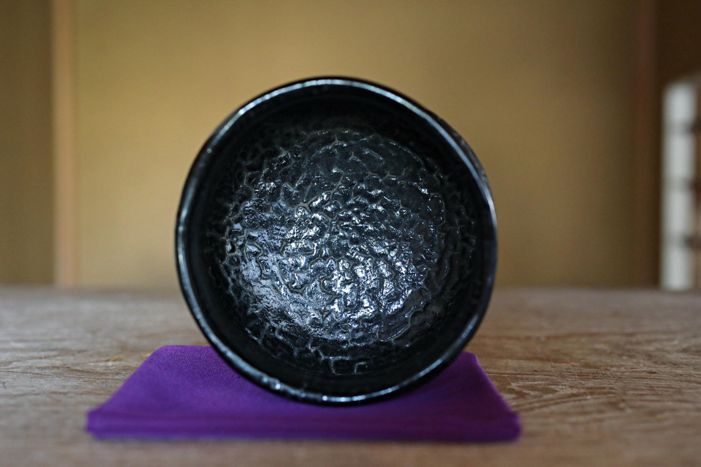 A black bowl with a textured surface sits on a purple cloth on a wooden surface.