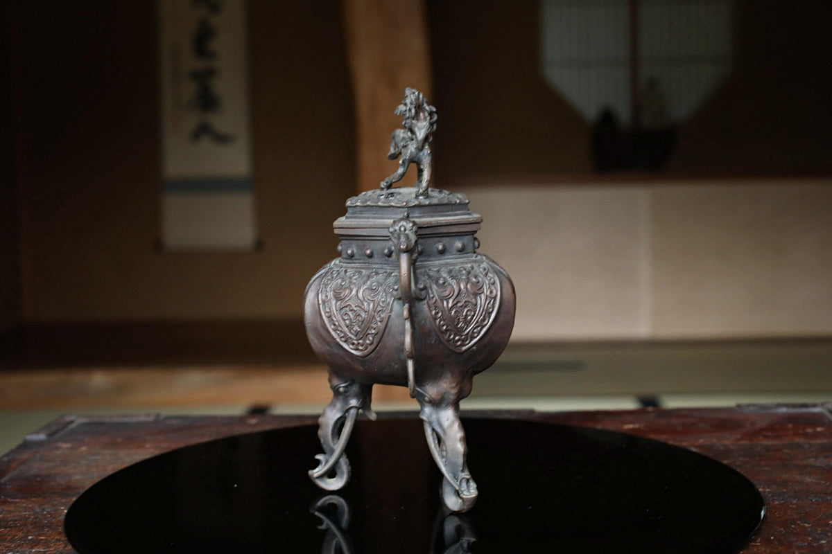 A decorative metal incense burner with a figurine on top, placed on a black circular surface.
