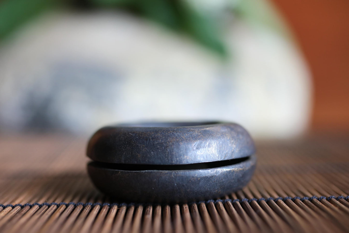 A black, round object sits on a bamboo mat, with a blurred background.