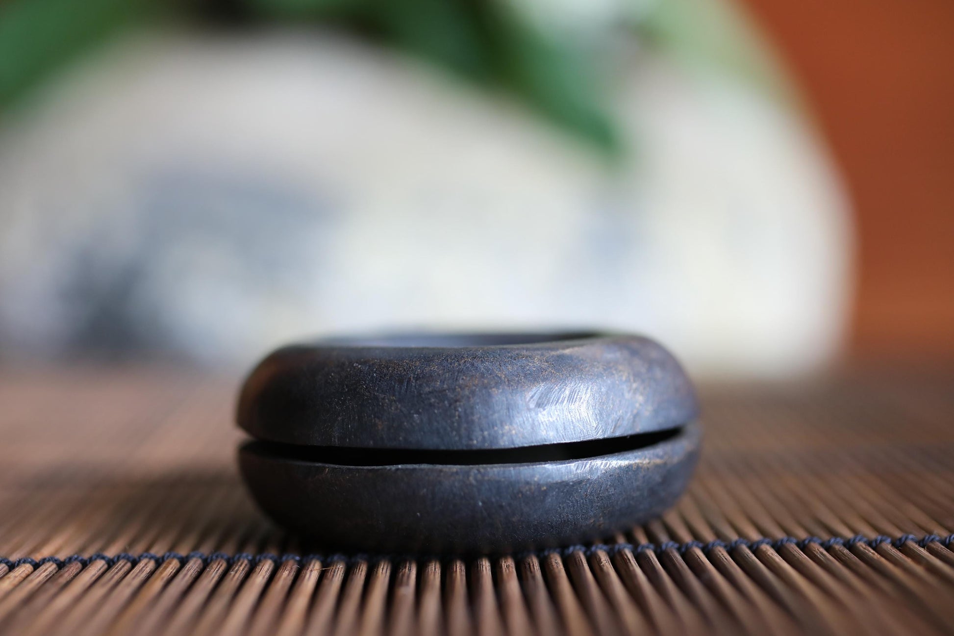 A black, round object sits on a bamboo mat, with a blurred background.
