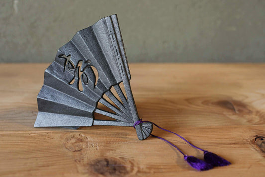 A black metal fan with a purple tassel is placed on a wooden surface.