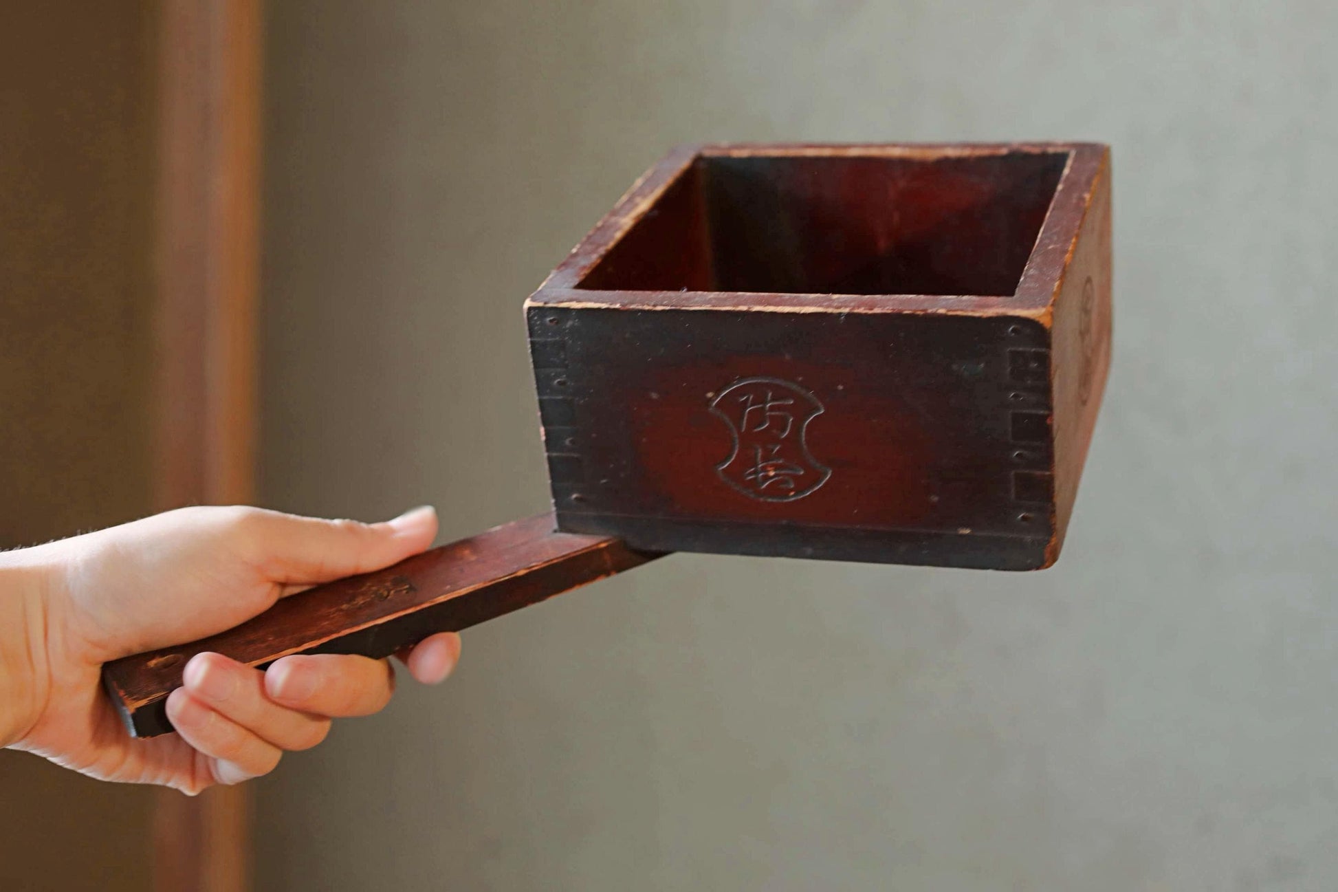 A hand is holding a wooden box with a lid, and the lid is being lifted off the box.