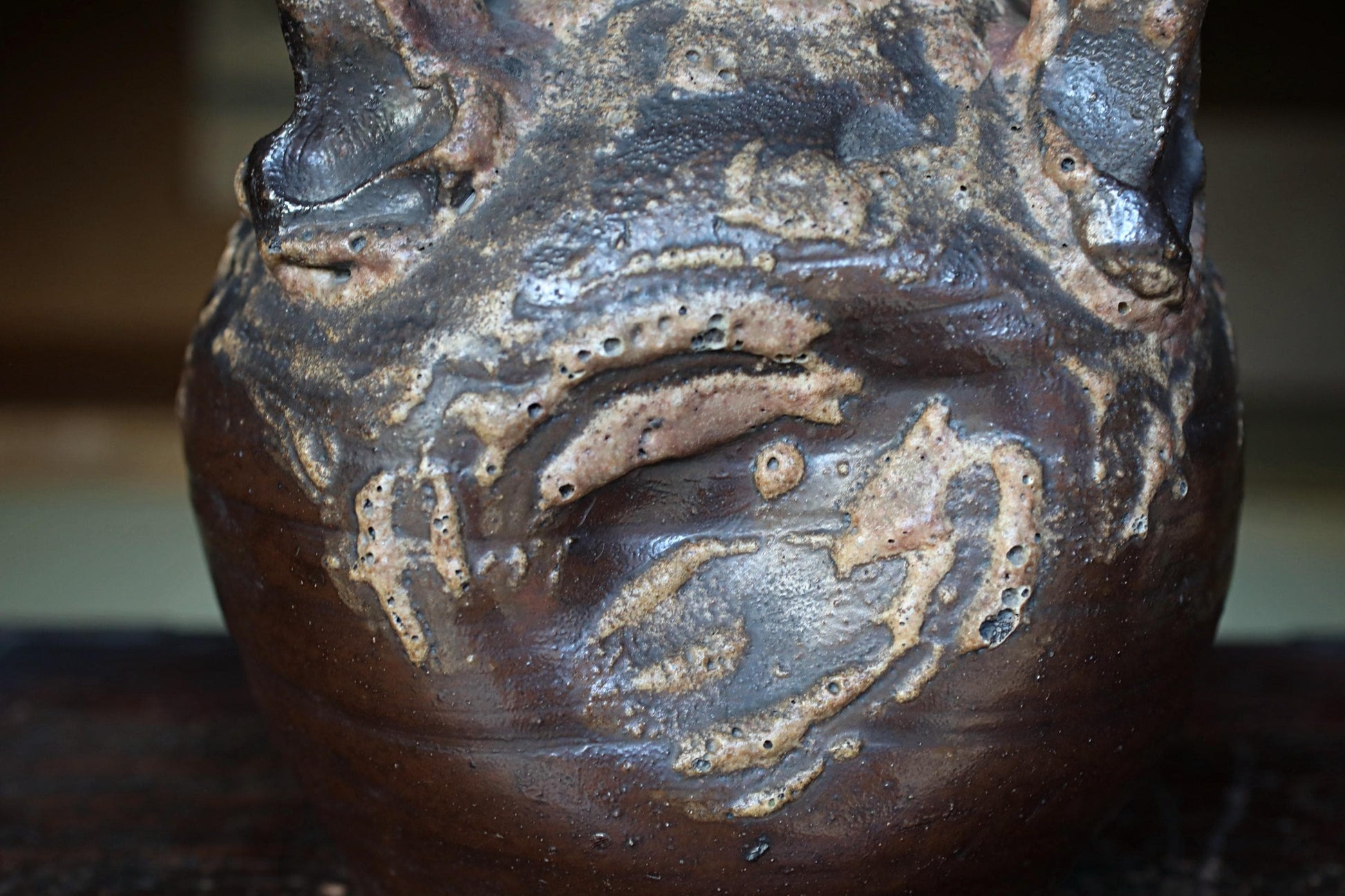 A close-up view of a dark brown ceramic vase with a textured surface, featuring a pattern of bubbles and cracks.