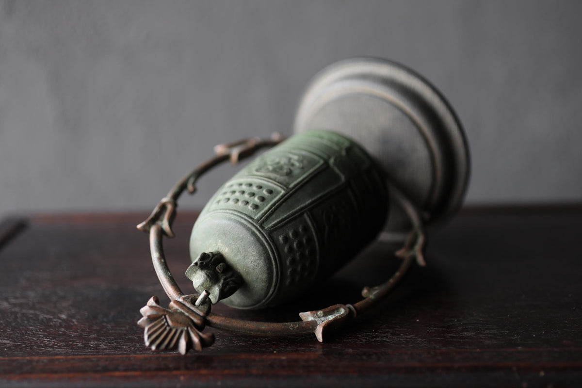 An antique green metal bell with a decorative design sits on a dark wooden surface.
