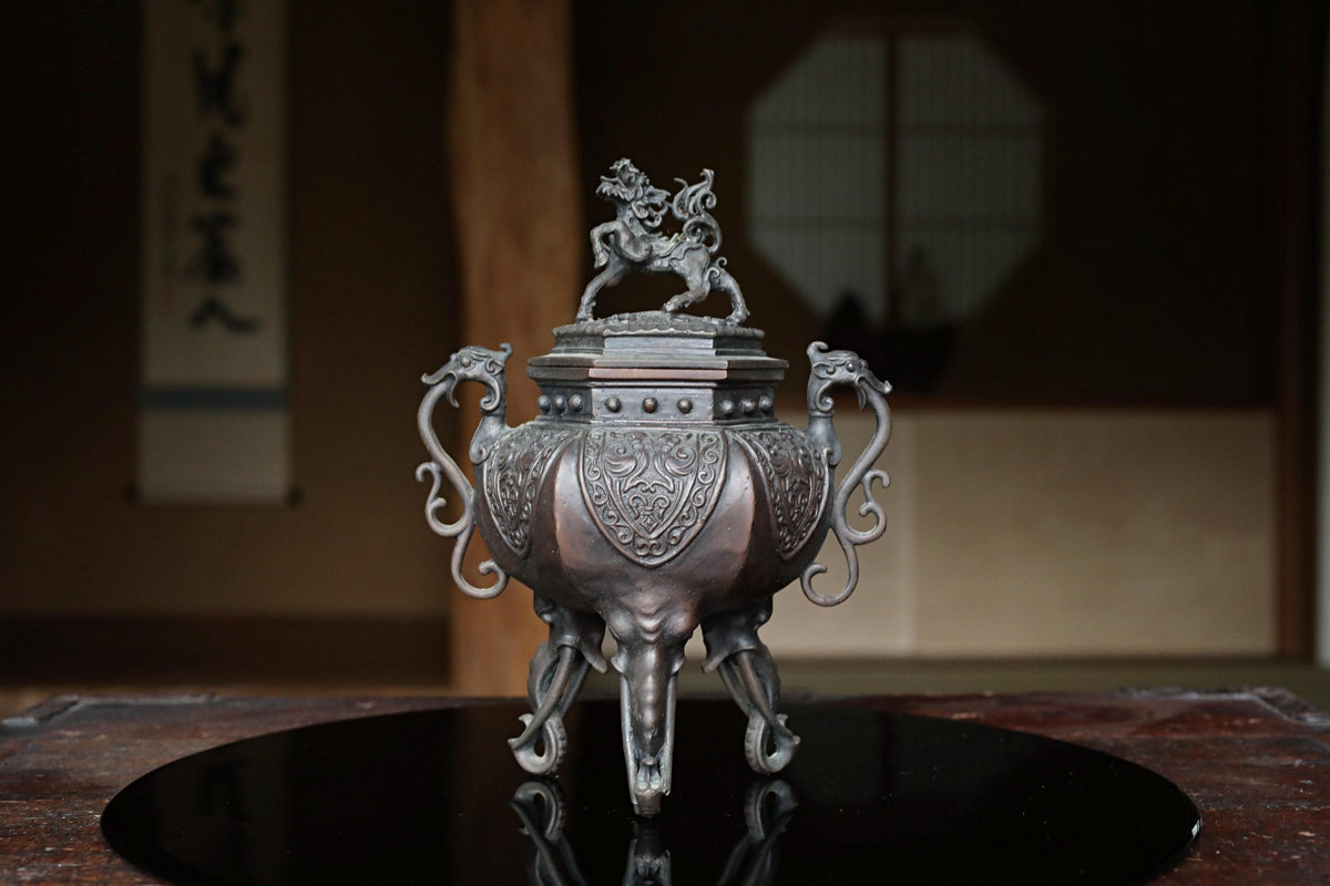 A decorative metal incense burner with an elephant-like design on the front, placed on a black circular surface.