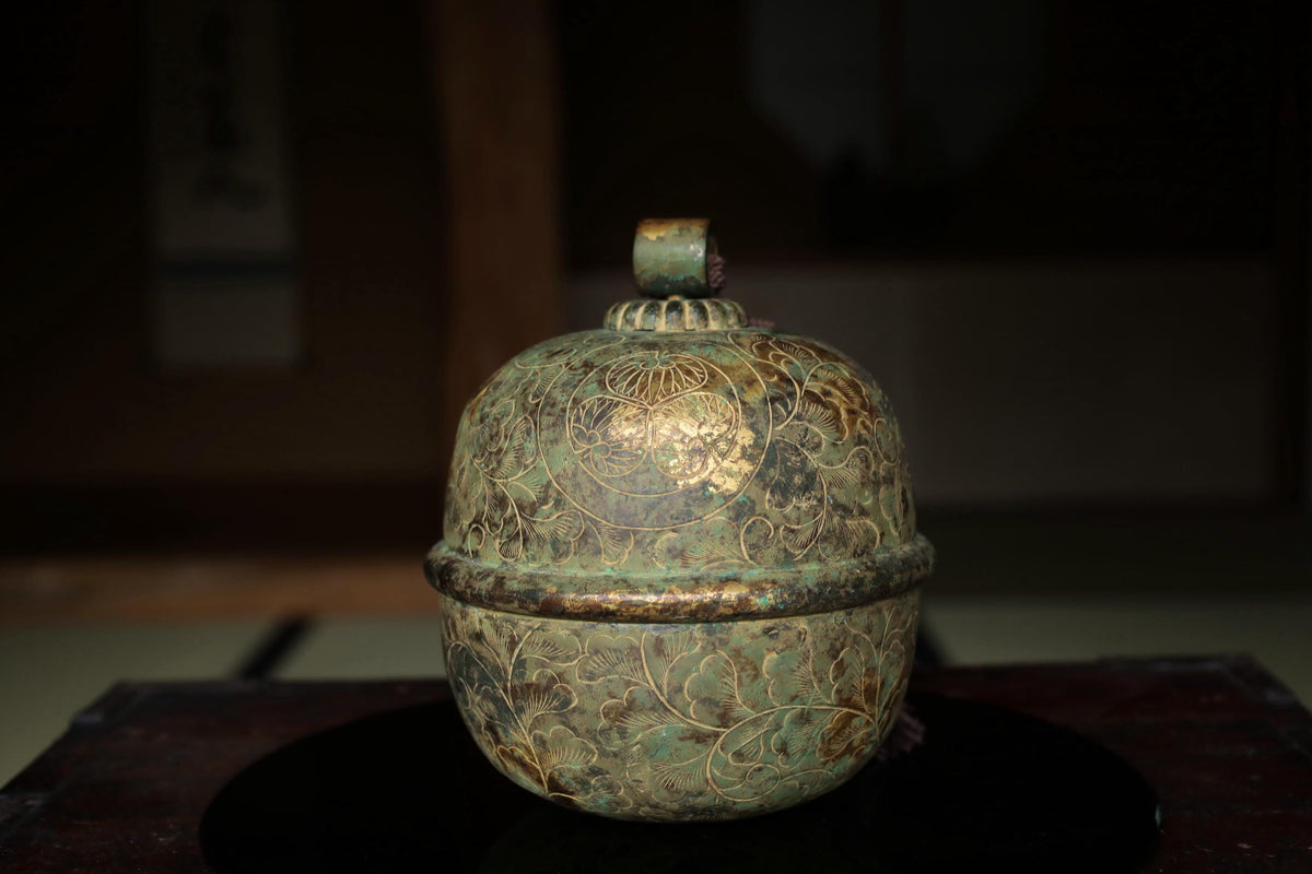 An ornate, green-colored vase with intricate designs sits on a dark surface.