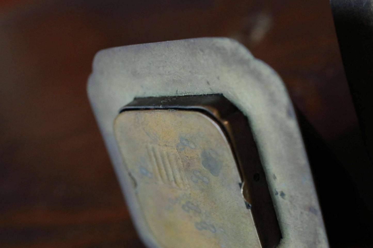 a close-up view of a metal object, possibly a small, square-shaped item, with a textured surface and a dark background.