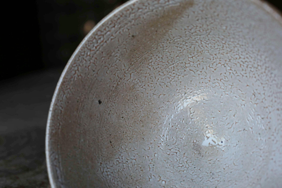 A close-up view of a white ceramic bowl with a textured surface, featuring a small hole in the center.