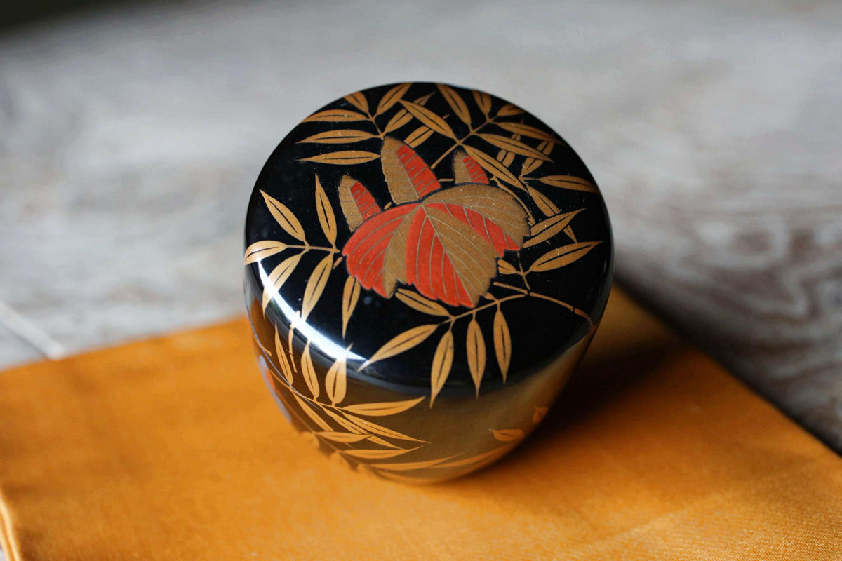 A decorative black and gold box with a floral design on top, placed on a yellow cloth.