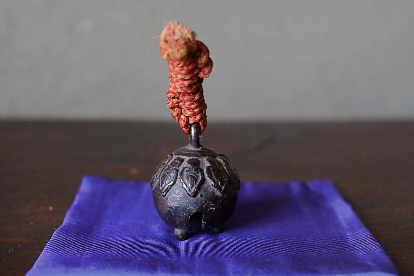 A small, ornate metal bell with a red string or cord hanging from the top, placed on a blue cloth or fabric.