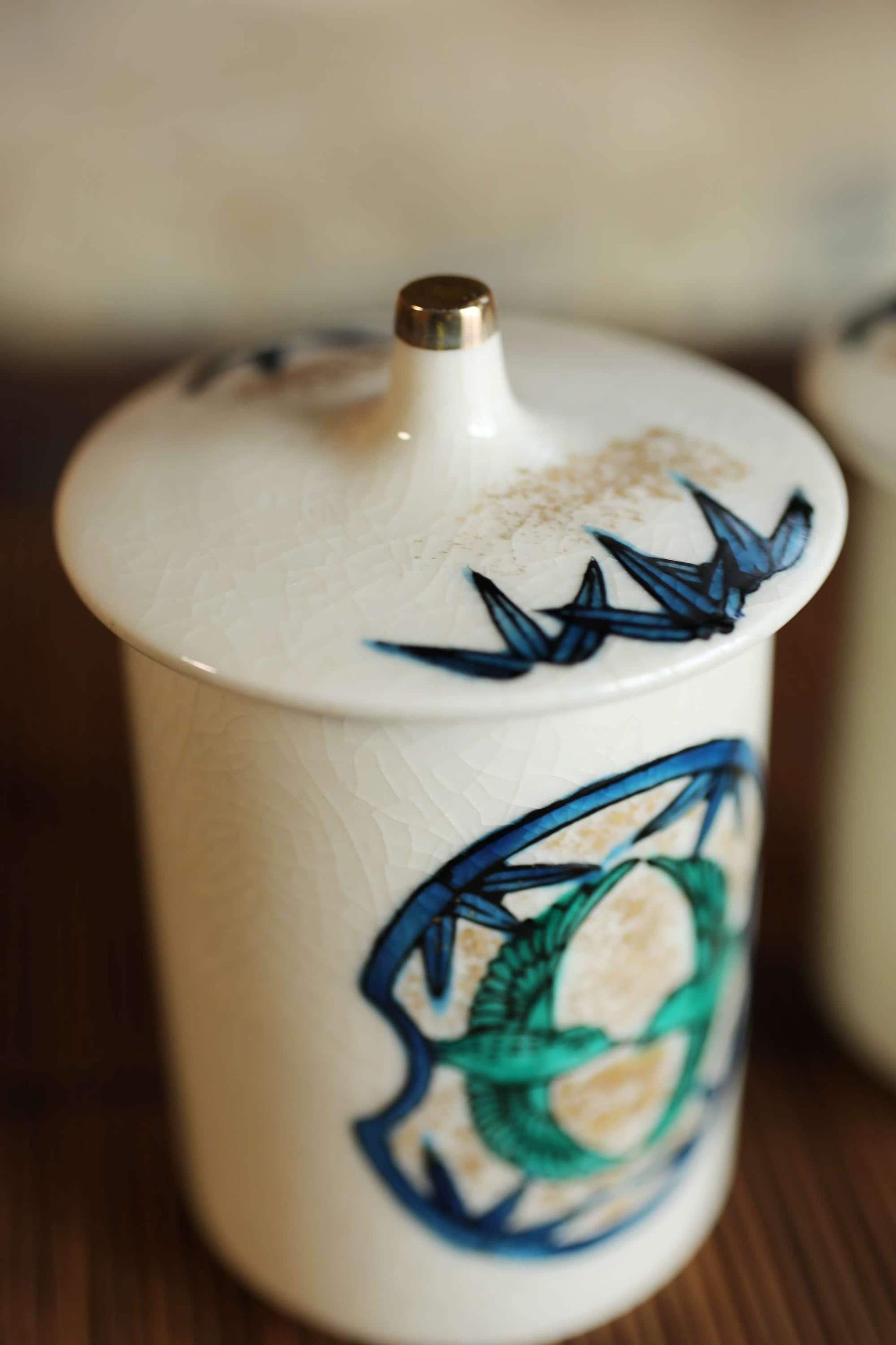 A white ceramic jar with a blue and green design on it, placed on a wooden surface.