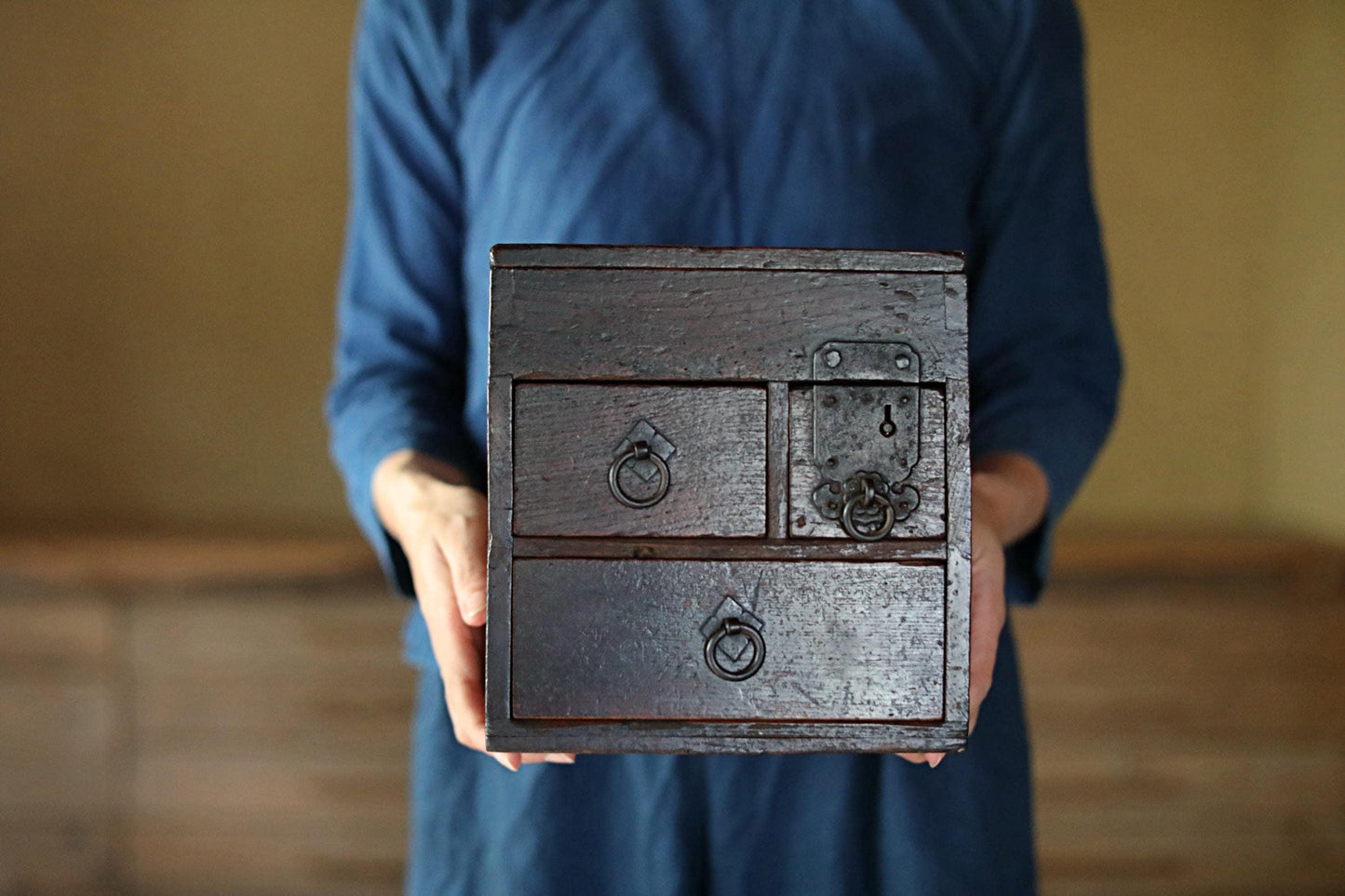 A person wearing a blue shirt is holding a wooden box with two drawers in their hands.