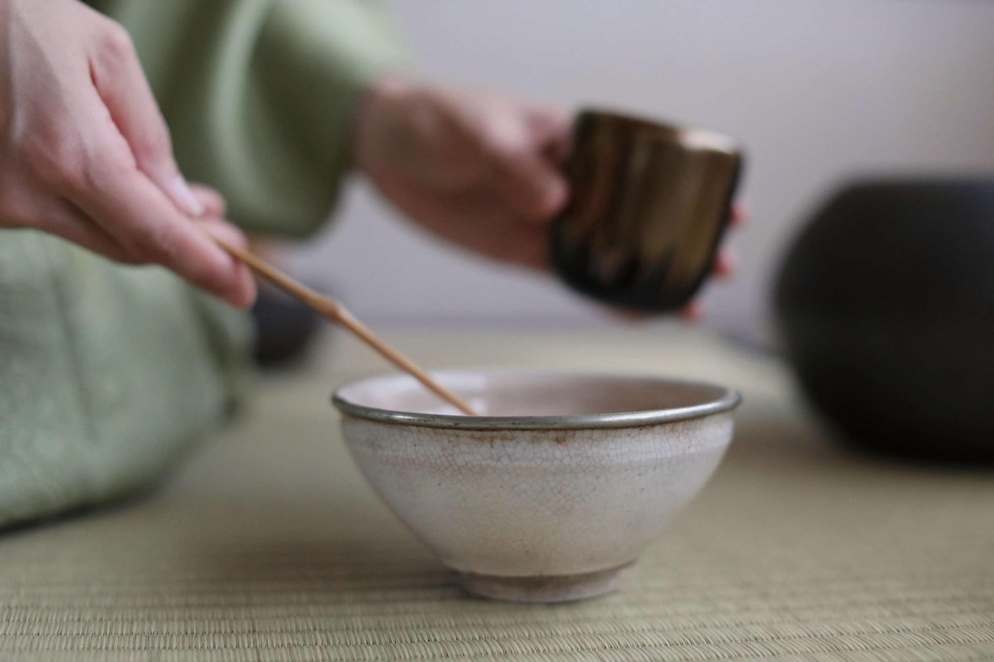A person's hands are holding a small white bowl and a spoon, preparing to stir something in the bowl.