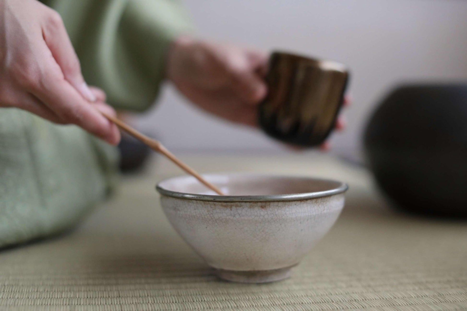 A person's hands are holding a small white bowl and a spoon, preparing to stir something in the bowl.