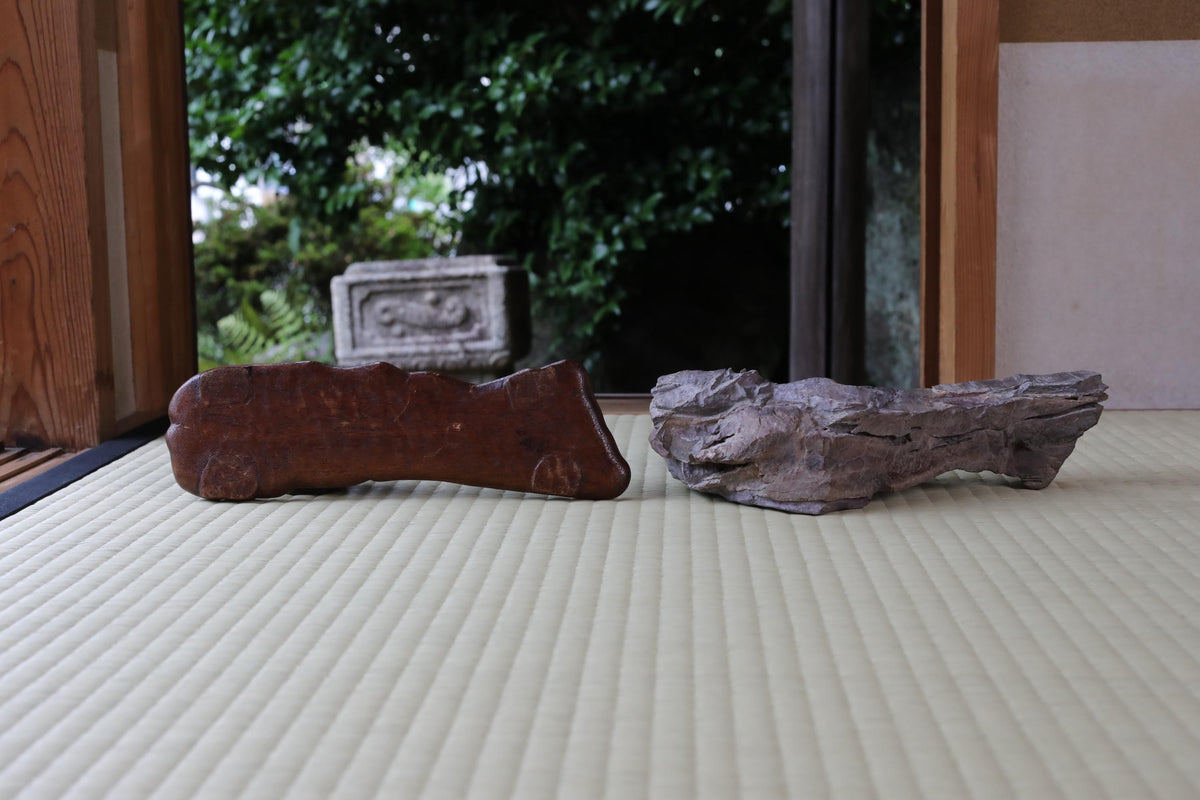 two wooden objects placed on a white surface, with a blurred background of greenery.