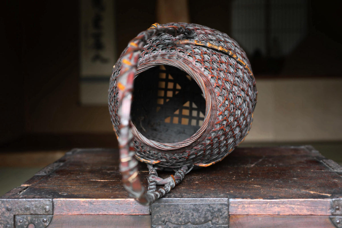 An old, intricately woven basket with a wooden handle rests on a wooden surface.