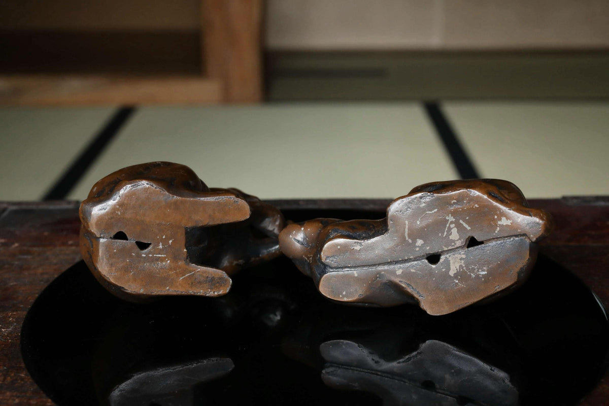 Two bronze figurines of a cat sitting on a wooden surface.