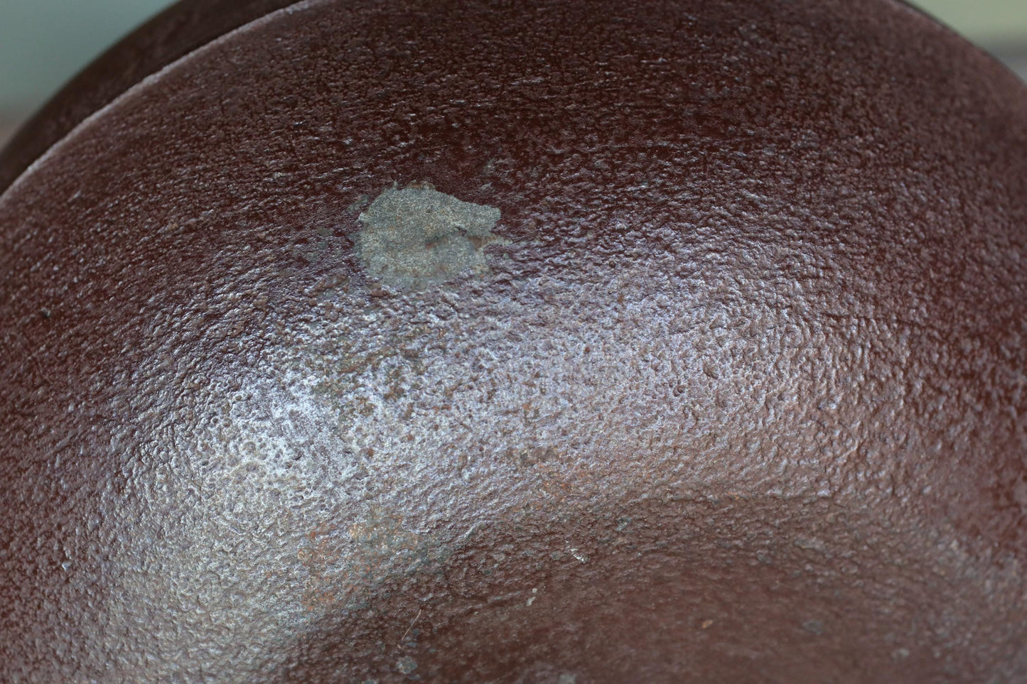 a close-up view of a textured brown surface, possibly a bowl or a piece of pottery. There is a small, circular hole or blemish in the center of the surface.
